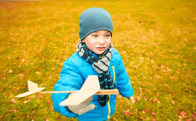 otoño, infancia, sueño, ocio y concepto de la gente - niño feliz jugando con un avión de juguete de madera al aire libre