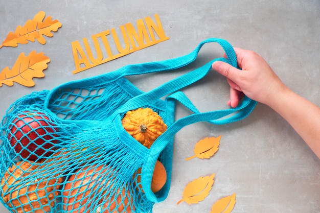 Otoño plano con bolsa de hilo turquesa con calabazas naranjas, parte superior en piedra gris