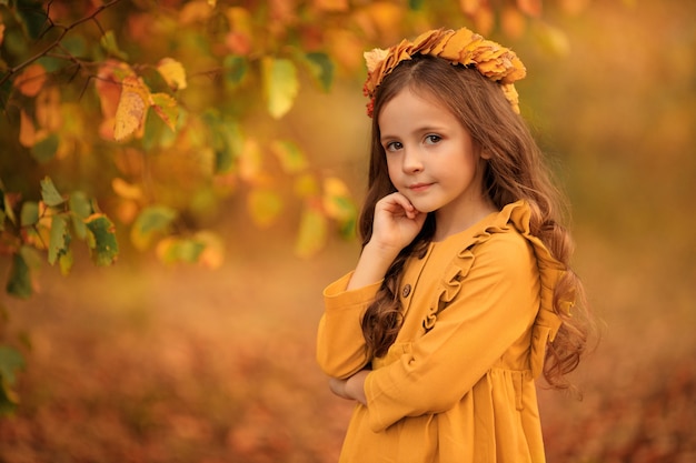 Otoño retrato de una hermosa niña caminando en el parque con una corona de hojas amarillas