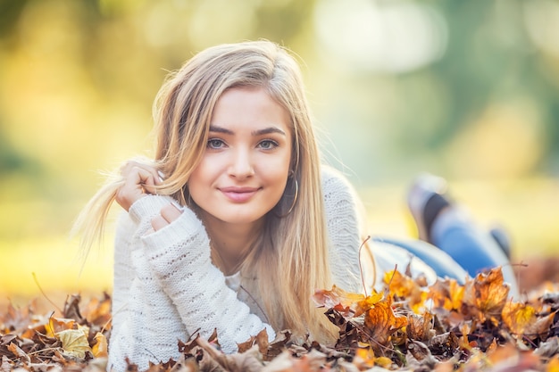 Otoño retrato de mujer joven acostada sobre hojas de arce en el parque.