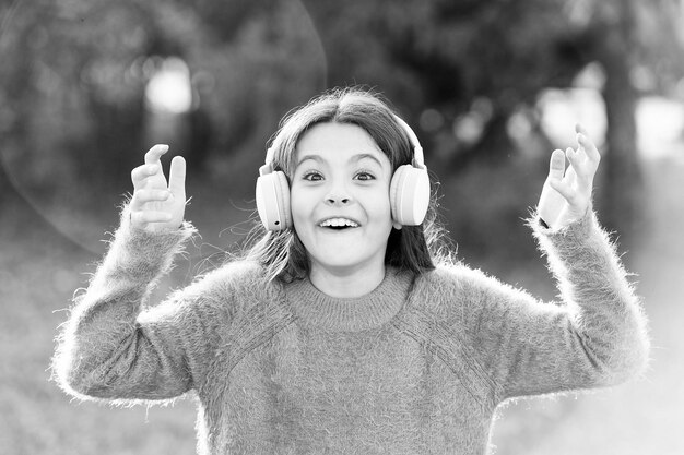 Ouça com estilo Menina usando fones de ouvido Criança feliz gosta de ouvir música em movimento Menina adorável ao ar livre Tudo o que ela quer ouvir é música