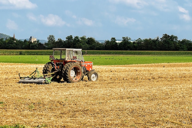 Ouhans, Francia - 1 de septiembre de 2016: Tractor y trabajador con arado haciendo trabajo estacional agrícola en el campo.