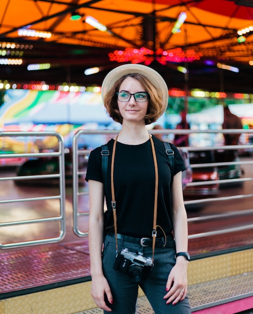 Ã Â oung hipster mujer con sombrero y gafas de sol con cámara retro en el parque de atracciones