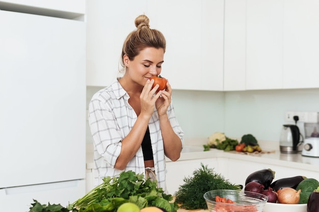 Oung hübsche Frau mit schnüffelnden reifen Tomaten während des Kochens