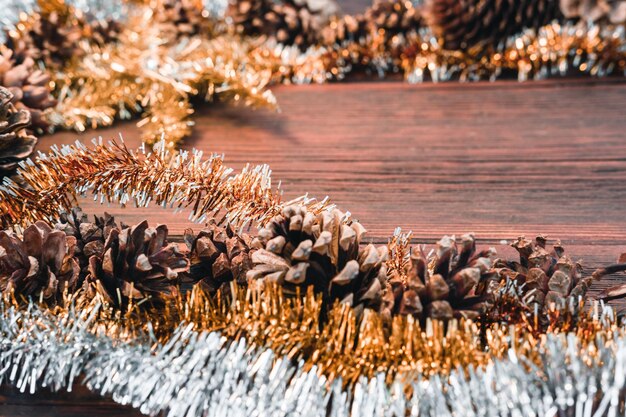 Ouro laranja amarelo e ouropel brilhante prateado em um cartão de Natal de fundo de madeira com pinhas