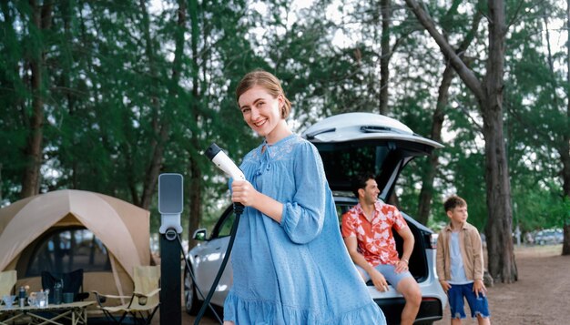 Outdoor-Abenteuer und Familienurlaub, Camping am Meer, Reisen mit dem umweltfreundlichen Auto. Fröhliche Frau oder Mutter, die auf dem Campingplatz Perpetual zeigt und auf die Ladestation für Elektrofahrzeuge zeigt, mit verspielter und fröhlicher Haltung