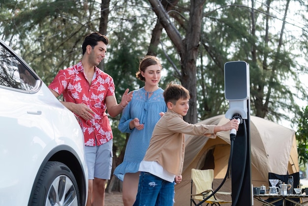 Outdoor-Abenteuer und Familienurlaub, Camping in der Natur, Reisen mit einem umweltfreundlichen Auto für eine nachhaltige Zukunft. Schönes Familien-Elektroauto mit Ladestation auf dem Campingplatz Perpetual