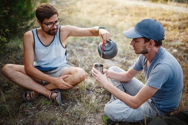 Outdoor-Bild eines jungen Entdeckers, der nach dem Trekking ein heißes Getränk in den Bergen trinkt und sich entspannt