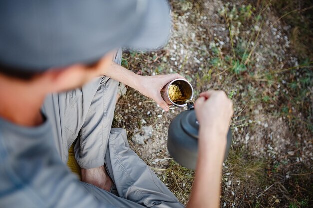 Outdoor-Bild eines jungen Entdeckers, der nach dem Trekking ein heißes Getränk in den Bergen trinkt und sich entspannt