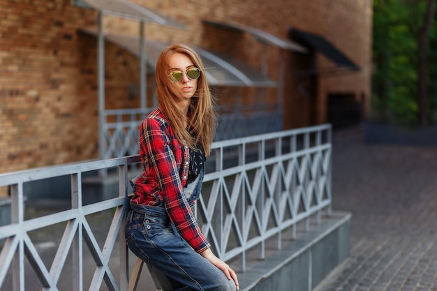 Outdoor-Lifestyle-Porträt eines hübschen jungen Mädchens, das im Hipster-Swag-Grunge-Stil auf urbanem Hintergrund trägt