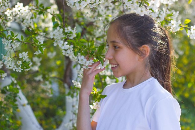 Outdoor-Nahaufnahme eines jungen Mädchens, das auf der Straße in der Nähe eines blühenden Baums mit weißen Blumen posiert