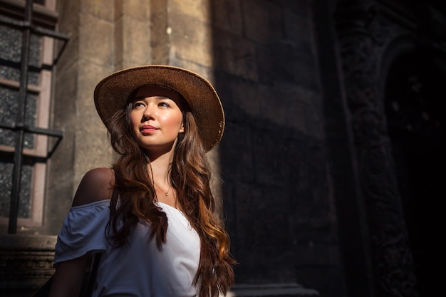 Outdoor-Porträt der jungen touristischen Frau, die auf der alten Stadtstraße geht. Mädchen, das bei Sonnenuntergang antike Architektur betrachtet