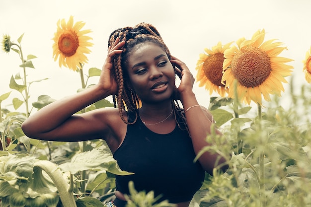 Outdoor-Porträt der schönen glücklichen gemischten Rasse Afroamerikanerin in einem Feld gelber Blumen bei Sonnenuntergang goldene Abendsonne