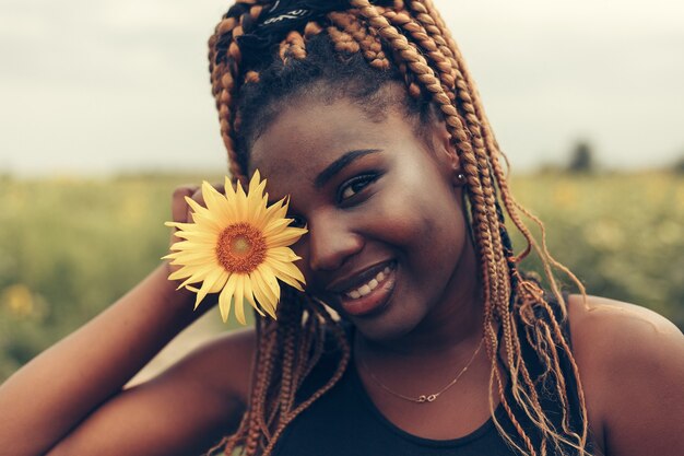 Outdoor-Porträt der schönen glücklichen gemischten Rasse Afroamerikanerin in einem Feld gelber Blumen bei Sonnenuntergang goldene Abendsonne