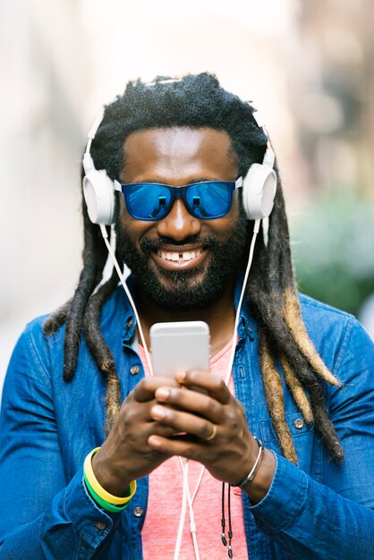 Outdoor-Porträt des hübschen afrikanischen jungen Mannes, der Nachricht schreibt und Musik hört.