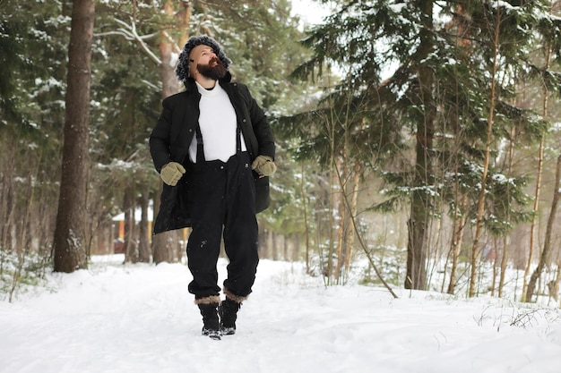 Outdoor-Porträt eines gutaussehenden Mannes in Mantel und Schal. Bärtiger Mann im Winterwald.