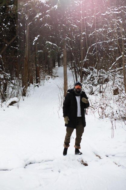 Outdoor-Porträt eines gutaussehenden Mannes in Mantel und Schal. Bärtiger Mann im Winterwald.