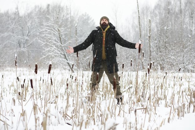 Outdoor-Porträt eines gutaussehenden Mannes in Mantel und Schal. Bärtiger Mann im Winterwald.