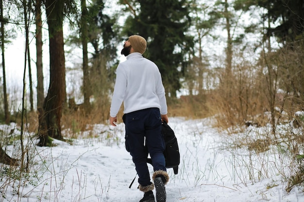 Outdoor-Porträt eines gutaussehenden Mannes in Mantel und Schal. Bärtiger Mann im Winterwald.