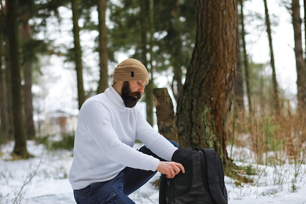 Outdoor-Porträt eines gutaussehenden Mannes in Mantel und Schal. Bärtiger Mann im Winterwald.