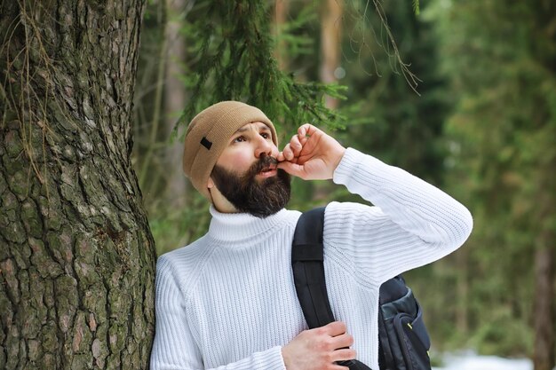 Outdoor-Porträt eines gutaussehenden Mannes in Mantel und Schal. Bärtiger Mann im Winterwald.