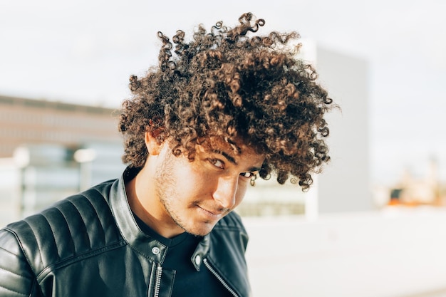 Foto outdoor-porträt eines jungen mannes mit einem lebhaften und sympathischen aussehen mit lockigem haar, das in die kamera schaut