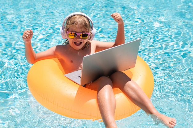 Outdoor-Sommer-Business-Kind-Remote-Arbeiten am Laptop im Pool Kleiner Geschäftsmann, der online arbeitet