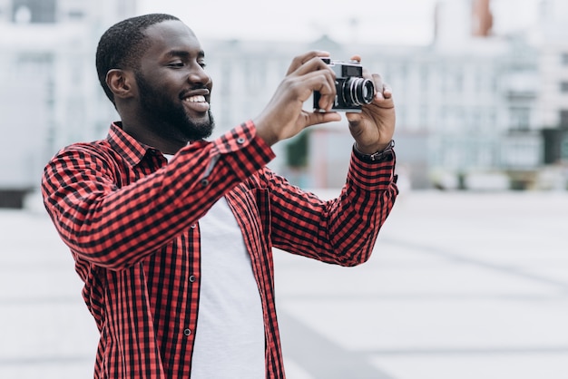 Outdoor Sommer lächelnd Lifestyle Porträt von gut aussehend und glücklich Afro American Tourist Spaß in der Stadt in Europa mit Kamera Reise Foto von Fotografen machen Bilder in Hipster-Stil