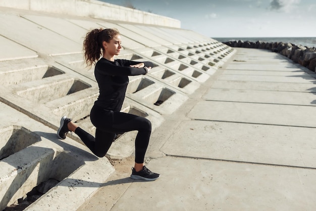 Outdoor-Workout-Konzept Fitte schlanke Frau mit lockigem Haar dehnt sich aus oder wärmt sich auf einer städtischen Böschung mit Betonplatten auf