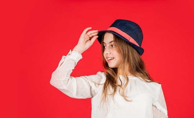 Outfit-Inspiration. Individueller Stil. Mädchen tragen Hut roten Hintergrund. Glückliches Kind mit Hut. Mode-Accessoire. Fühlen Sie sich schick. Accessoire-Kollektion für den Sommer. Lange Haare des Kindes tragen Hut. Zubehör-Shop.