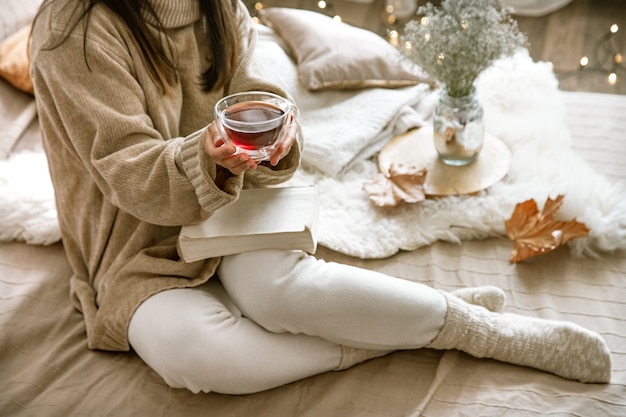 Foto outono aconchegante em casa, uma mulher com um livro e um chá a descansar. um estilo de vida aconchegante. partes do corpo na composição.