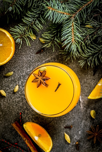 Outono, cocktails de inverno, ponche quente de inverno picante laranja com canela, estrelas de anis, cardamomo, cravo. Na mesa de pedra preta, com ingredientes e galhos de árvores de Natal, em copos. vista superior copyspace