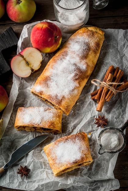 Outono em casa, cozimento de verão, bolos folhados. Strudel de maçã com nozes, passas, canela e açúcar em pó. Em uma velha mesa rústica de madeira. Fatiado, com ingredientes. Vista superior do espaço da cópia