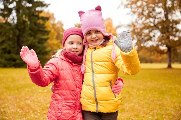 outono, infância, lazer e conceito de pessoas - duas meninas felizes acenando com a mão no parque outono