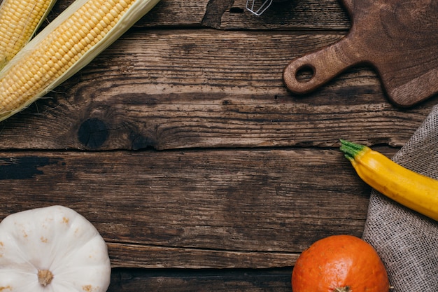 Outono legumes: abóboras e milho com folhas amarelas e cortar a tábua na madeira