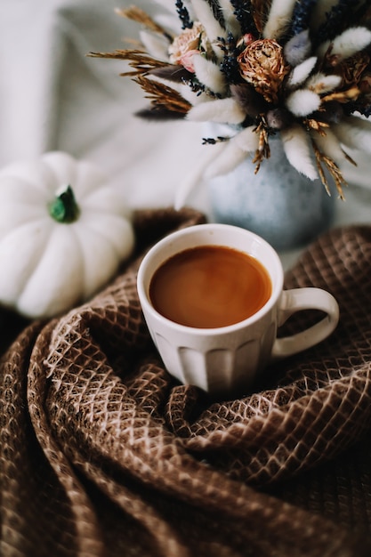 Outono natureza morta com uma xícara de café com flores e abóboras em uma manta aconchegante na cama elegante de outono ...