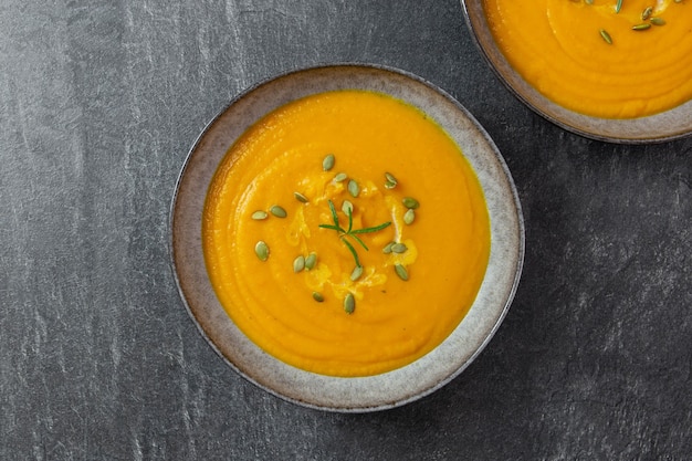 Outono sazonal de outono assado de abóbora e sopa de cenoura com creme e sementes de abóbora na superfície escura