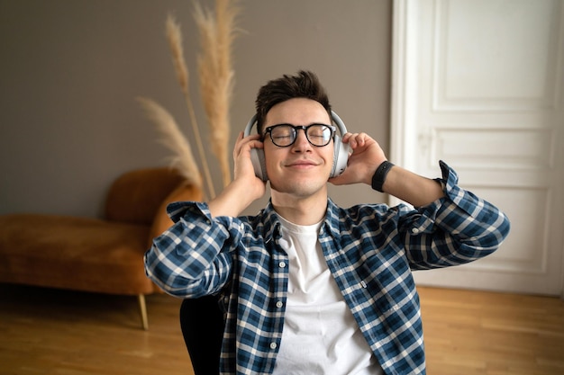 Foto ouve música calma em fones de ouvido sem fio, um homem de óculos está feliz e em equilíbrio de espírito