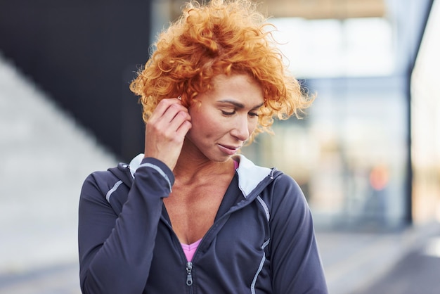 Ouvindo a música em fones de ouvido Retrato de uma jovem ruiva europeia que está ao ar livre