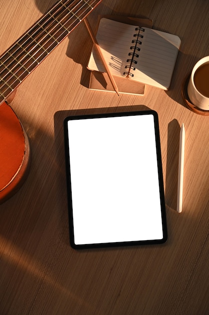 Overhead-Aufnahme von digitalem Tablet, Notebook, Kaffeetasse und Akustikgitarre auf Holzboden.