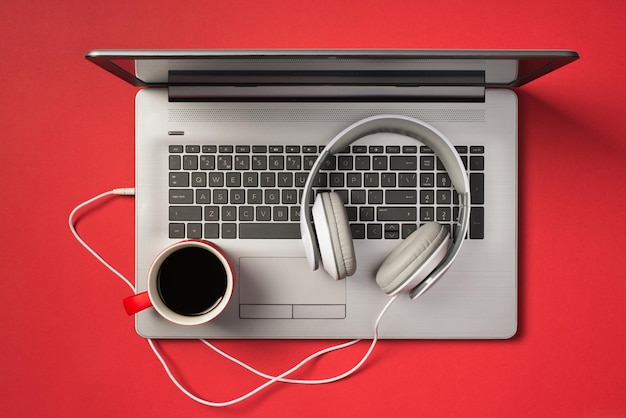 Overhead-Foto einer grauen Laptop-Tasse Kaffee und Kopfhörer isoliert auf dem roten Hintergrund