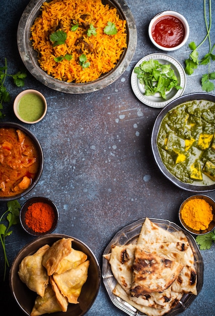 Overhead indischer traditioneller Gerichte und Vorspeisen: Hühnercurry, Pilaw, Naan-Brot, Samosas, Paneer, Chutney auf rustikalem Hintergrund. Tisch mit Auswahl an Speisen der indischen Küche, Platz für Text