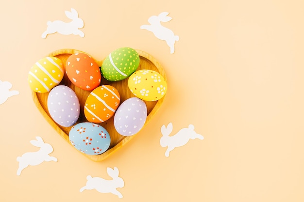 Overhead-Ostereier mit Kaninchenpapier, das in Herzform geschnitten ist, isoliert auf pastellfarbenem Hintergrund