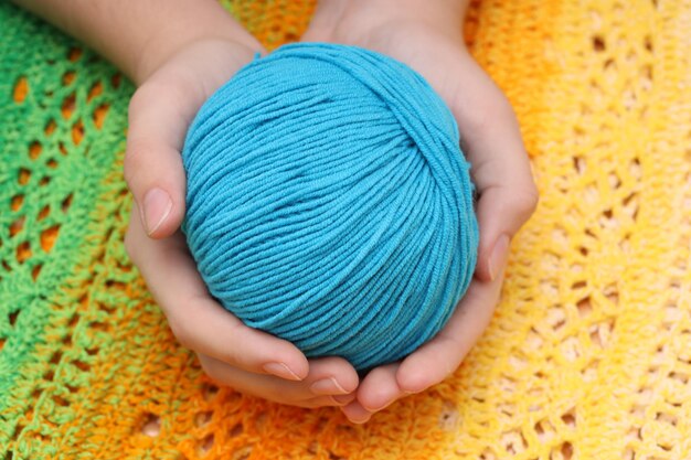 Ovillo de lana azul en las manos con el telón de fondo de un mantel de punto de color amarillo verdoso. Foto de alta calidad