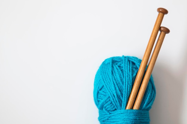 Un ovillo de lana azul turquesa con agujas de tejer de madera