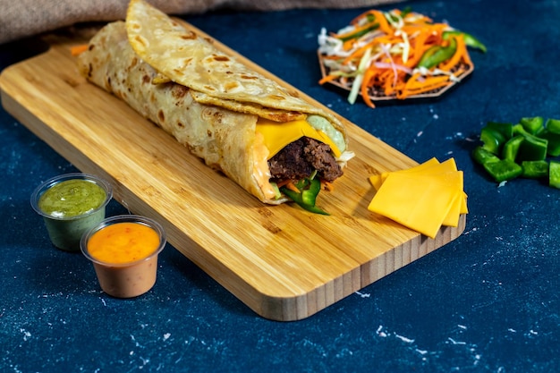 Ovo Cheesy Beef Overload shawarma Wrap com molho de salada e molho isolado placa de madeira vista lateral de fastfood