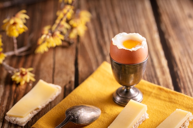 Ovo cozido em uma taça de prata com pão e queijo em uma mesa de madeira