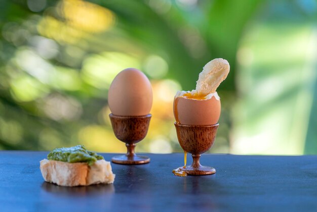 Ovo cozido macio em xícara de ovo com fatia de pão torrado na mesa de madeira no fundo da natureza closeup