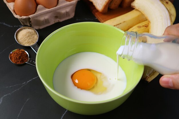 ovo cru em uma tigela de mistura sendo derramado por leite fresco para assar pudim de pão de banana