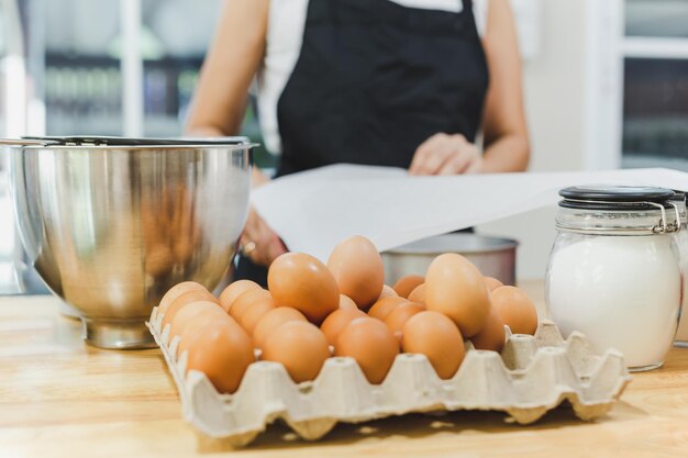 Ovo de galinha com ingredientes para assar na mesa com mulher padeiro em segundo plano